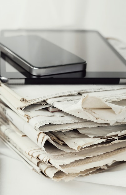 Stack of newspapers with digital tablet and smartphone