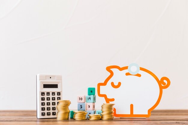 Stacked coins, math blocks, calculator and piggybank on wooden tabletop