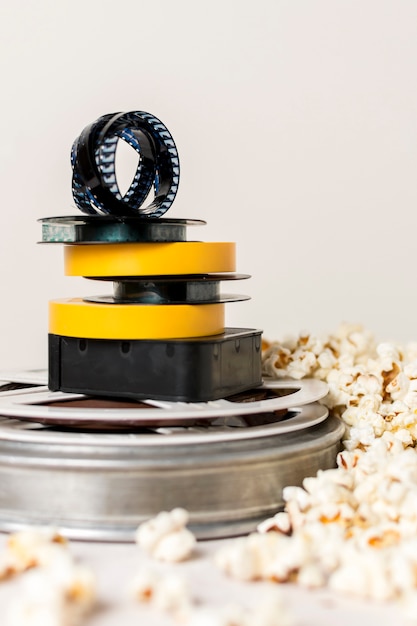 Free Photo stacked of film reels with film strip near the popcorn against white background