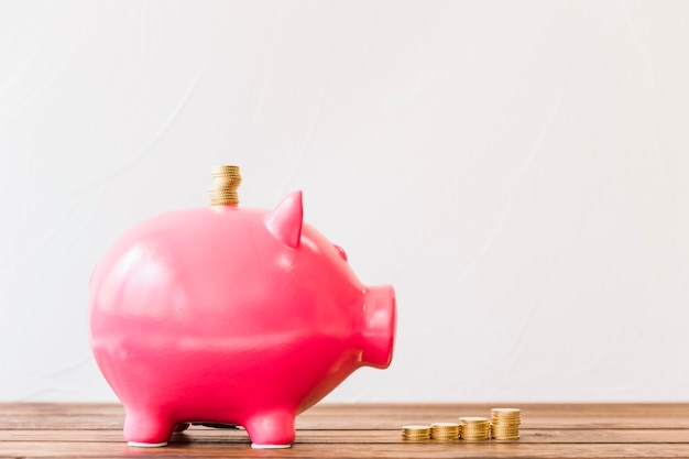 Stacked golden coins over piggybank slot on wooden surface