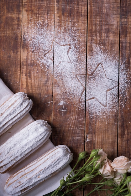 Free photo star shape drawn on wooden desk with baked eclairs and roses