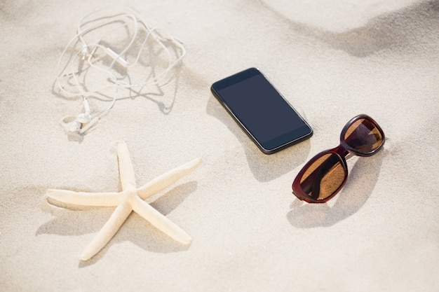 Free photo starfish, sunglasses, headphones and mobile phone kept on sand