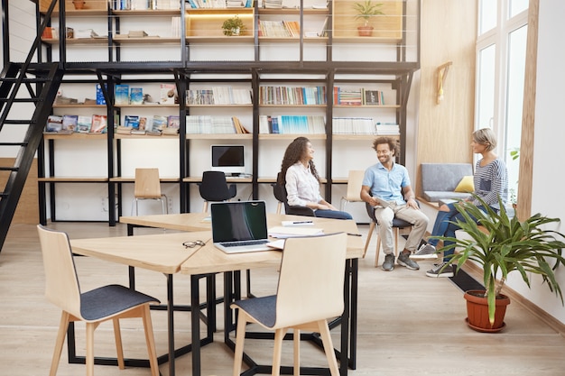 Free photo startup, business, teamwork concept. group of perspective young people on meeting in big modern library talking about profits of last project, looking through papers, smiling and having productive tim