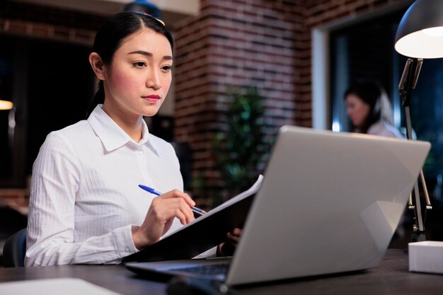 Startup project manager sitting in office workspace while analyzing accounting data. Confident smiling businesswoman with documentation clipboard reviewing financial documents.