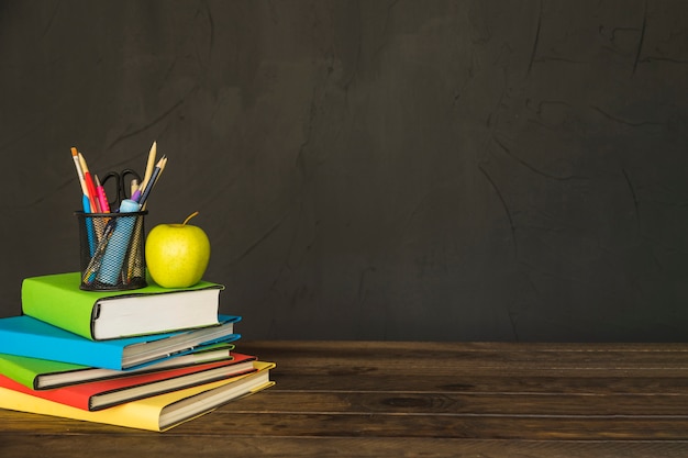 Stationary and apple on pile of books at table