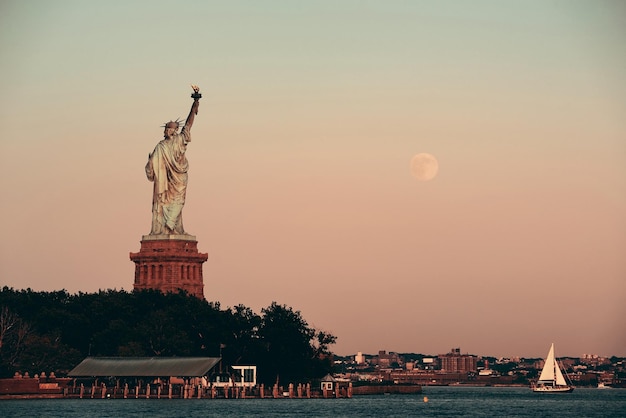 Free photo statue of liberty and full moon at sunset in new york city