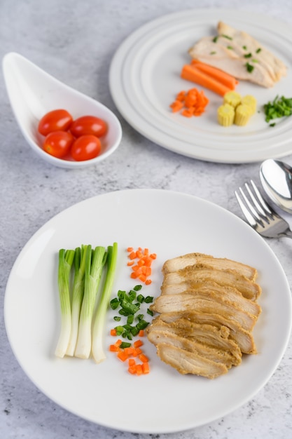 Steamed chicken breast on a white plate with spring onions and chopped carrots