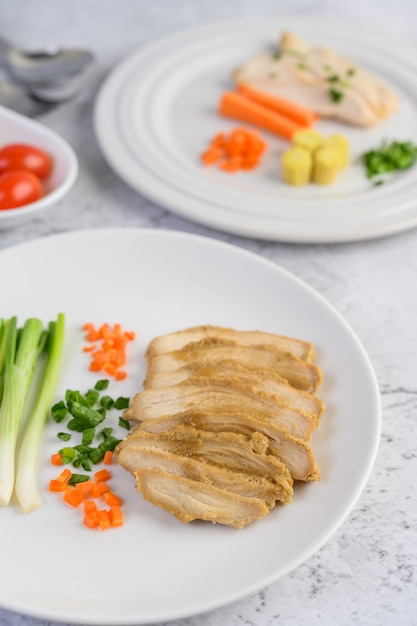 Steamed chicken breast on a white plate with spring onions and chopped carrots