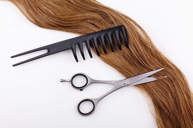 Steel scissors lie on the wave of silk brown hair with a black comb