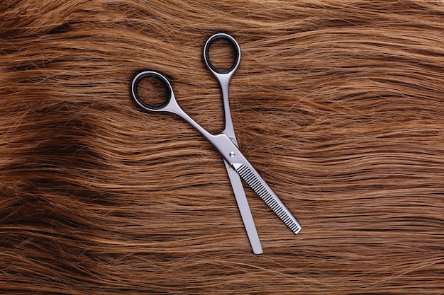 Free photo steel scissors lie on the wave of silk brown hair