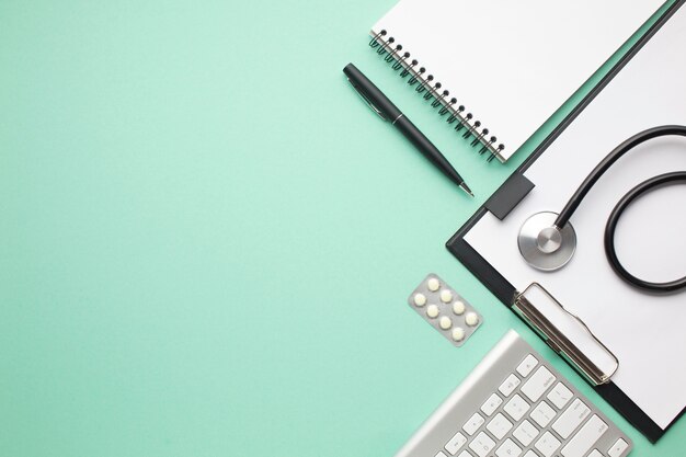 Stethoscope and blister pack of pill with office supplies over green background