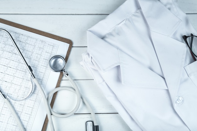 Free photo stethoscope,clipboard and doctor’s uniform on white neat wooden desk