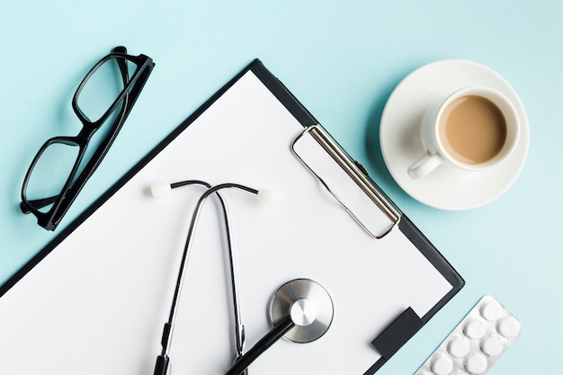 Free Photo stethoscope on clipboard with blister pack; spectacles and cup of coffee over desk