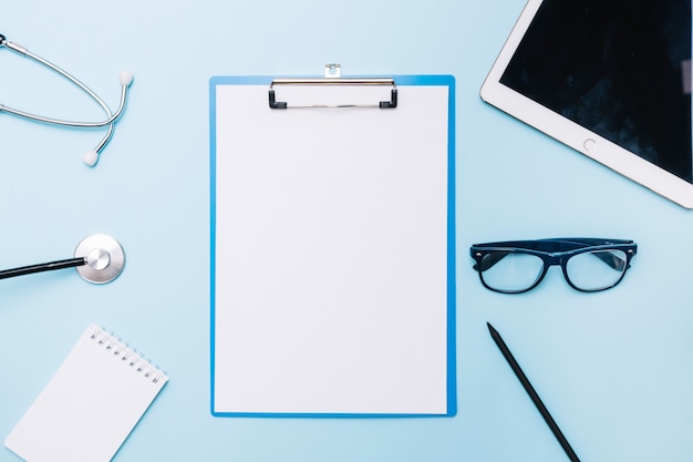 Stethoscope and glasses near clipboard and tablet