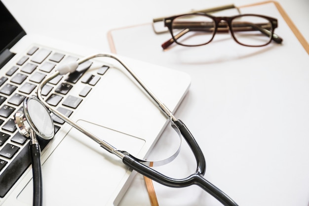 Stethoscope on laptop with clipboard and eyeglasses