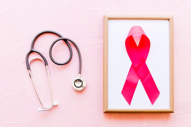 Stethoscope near the wooden frame with breast cancer awareness pink ribbon