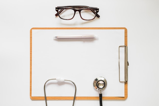 Free photo stethoscope; pen and eyeglasses on clipboard with paper over the white background