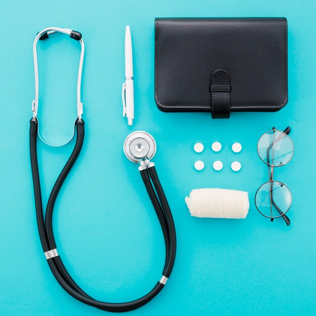 Stethoscope; pen; pills; diary; eyeglasses and bandage on blue background