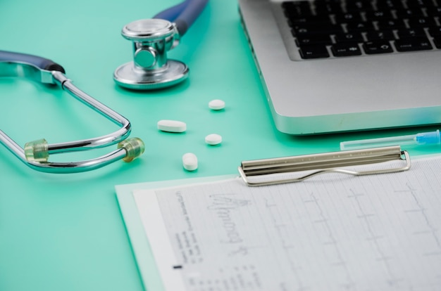 Free photo stethoscope; pills laptop and medical report on clipboard over the colored backdrop