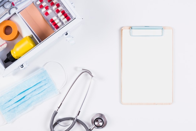 Stethoscope; surgical mask and clipboard with first aid kit on white background