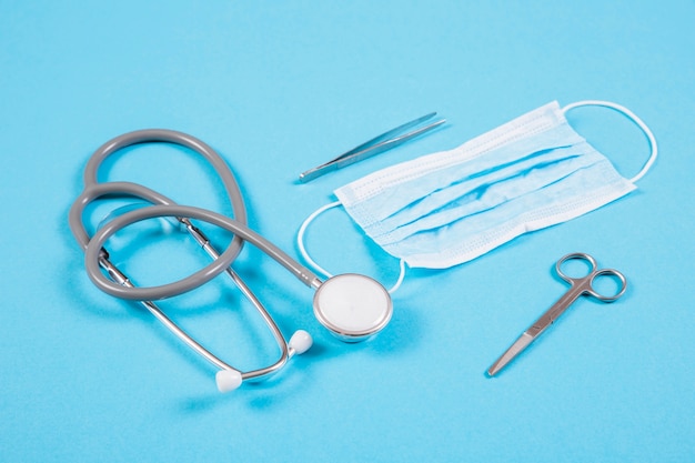 Free photo stethoscope; surgical mask; scissor and tweezers on colored background