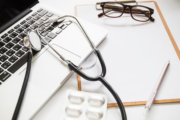 Stethoscope with laptop; clipboard; eyeglasses and pen on clipboard