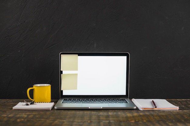 Sticky note on white blank screen laptop with coffee mug and stationeries over the wooden table