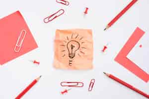 Free photo sticky note with drawn light bulb and office supplies over white background