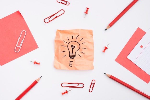 Sticky note with drawn light bulb and office supplies over white background