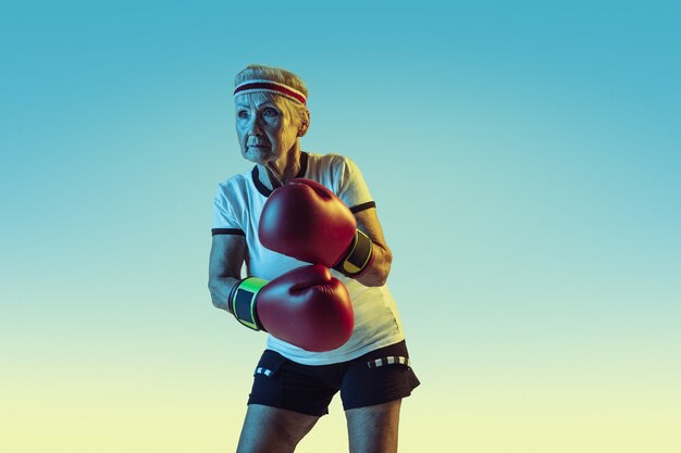 Still kicking. Senior woman in sportwear boxing on gradient