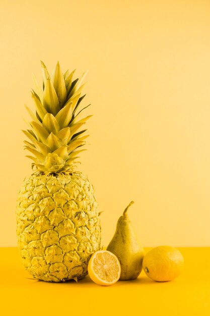 Still life of pineapple; lemon and pears against yellow backdrop