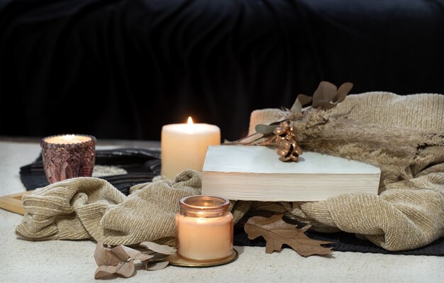 Still life on the table a book, a candle, tea on the space of a dark sofa. Autumn coziness concept.