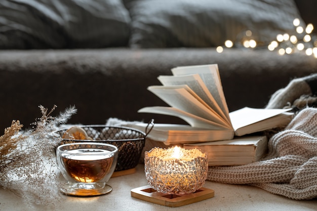 Still life with a cup of tea, books and a burning candle in a beautiful candlestick. Home comfort concept.