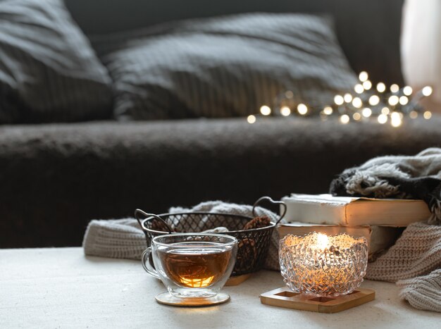 Still life with a cup of tea, a teapot, books and a burning candle in a candlestick with bokeh.