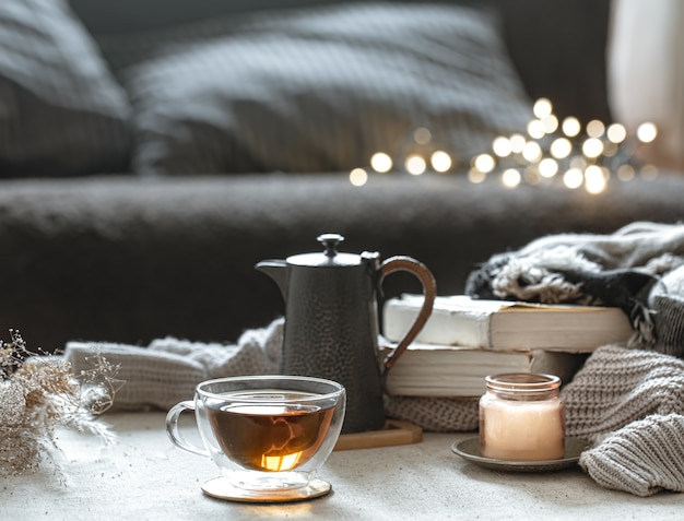 Still life with a cup of tea, a teapot, books and a candle in a candlestick with bokeh.