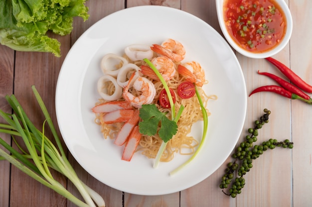 Stir-fried instant noodle with prawn and crab stick along  in a white dish.