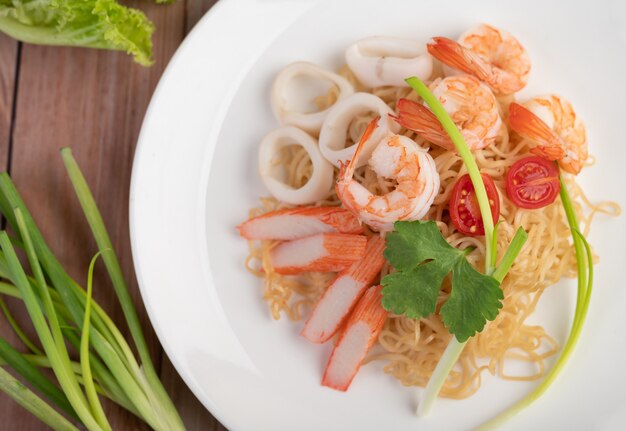 Stir-fried instant noodle with prawn and crab stick along  in a white dish.