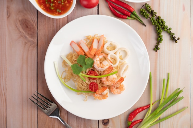 Stir-fried instant noodle with prawn and crab stick along  in a white dish.