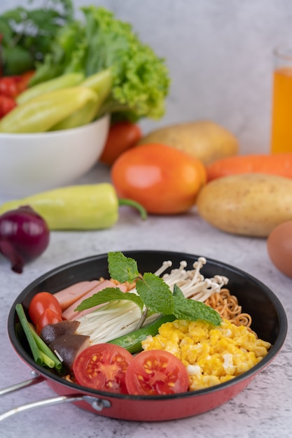 Stir fried noodle that combines corn, golden needle mushroom, tomato, sausage, edamame and spring onions in a frying pan.