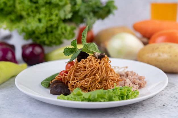 Free photo stir-fried noodles with minced pork, edamame, tomatoes and mushrooms in a white plate.