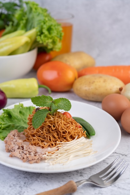 Stir-fried noodles with minced pork, edamame, tomatoes and mushrooms in a white plate.