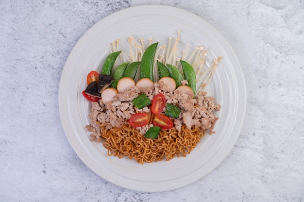 Stir-fried noodles with minced pork, edamame, tomatoes and mushrooms in a white plate.