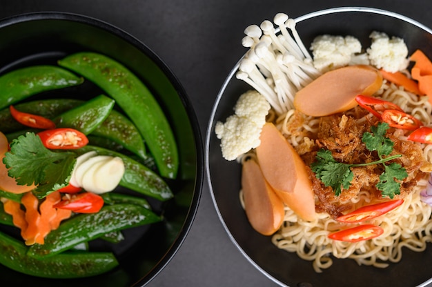 Free photo stir-fried peas in a frying pan and noodles spicy in the bowl with ingredients on black cement surface.