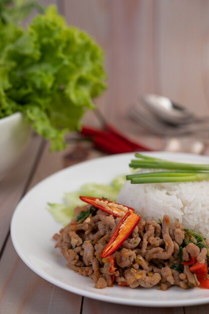 Stir fried pork with basil, fried egg in a white dish .