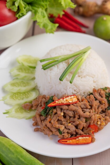 Stir fried pork with basil, fried egg in a white dish .