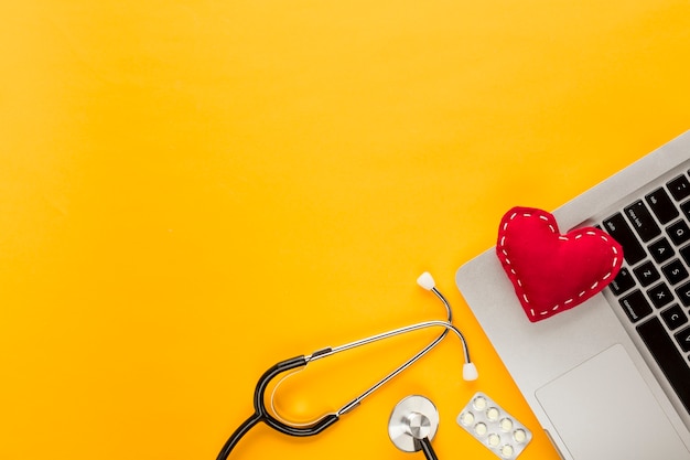 Free photo stitched heart shape on laptop with stethoscope; blister packed tablet on yellow background