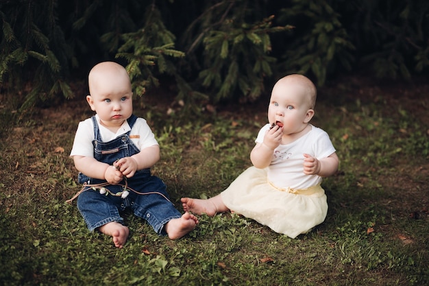 Free photo stock photo of adorable little babies sitting on the grass in the forest. little brother and sister eating berries while sitting on green grass in the forest.