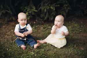 Free photo stock photo of adorable little babies sitting on the grass in the forest. little brother and sister eating berries while sitting on green grass in the forest.