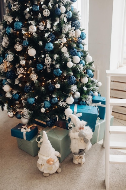 Free photo stock photo of beautiful decorated christmas tree with blue and silver and white balls and wrapped christmas presents under the tree. two santa claus figures under tree.