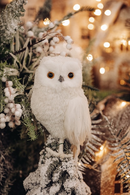 Free photo stock photo of a beautiful toy owl of white color sitting on fir tree branch with bokeh lights in the background.